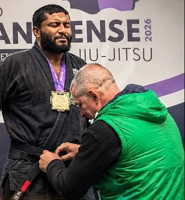 Mestre Danilo Rodacki amarrando a faixa preta no Lele, no pódio do Circuito Paranaense de Jiu-Jitsu 2026